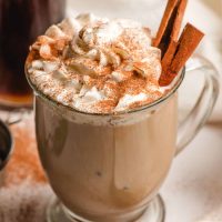 Glass mug filled with a cinnamon spiced latte and topped with whipped cream, cinnamon sticks, and ground cinnamon.