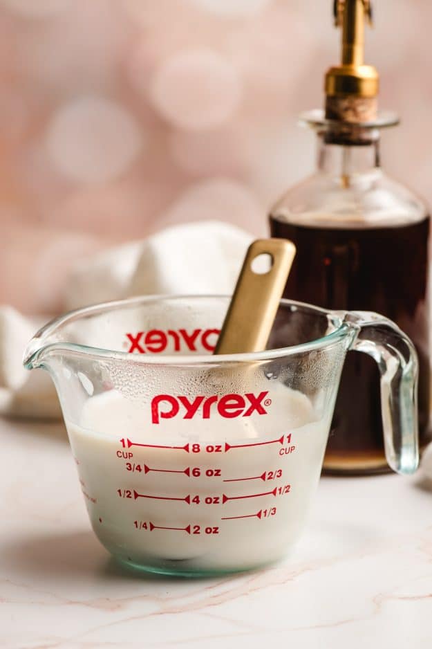 Milk mixed with cinnamon syrup in a measuring cup.
