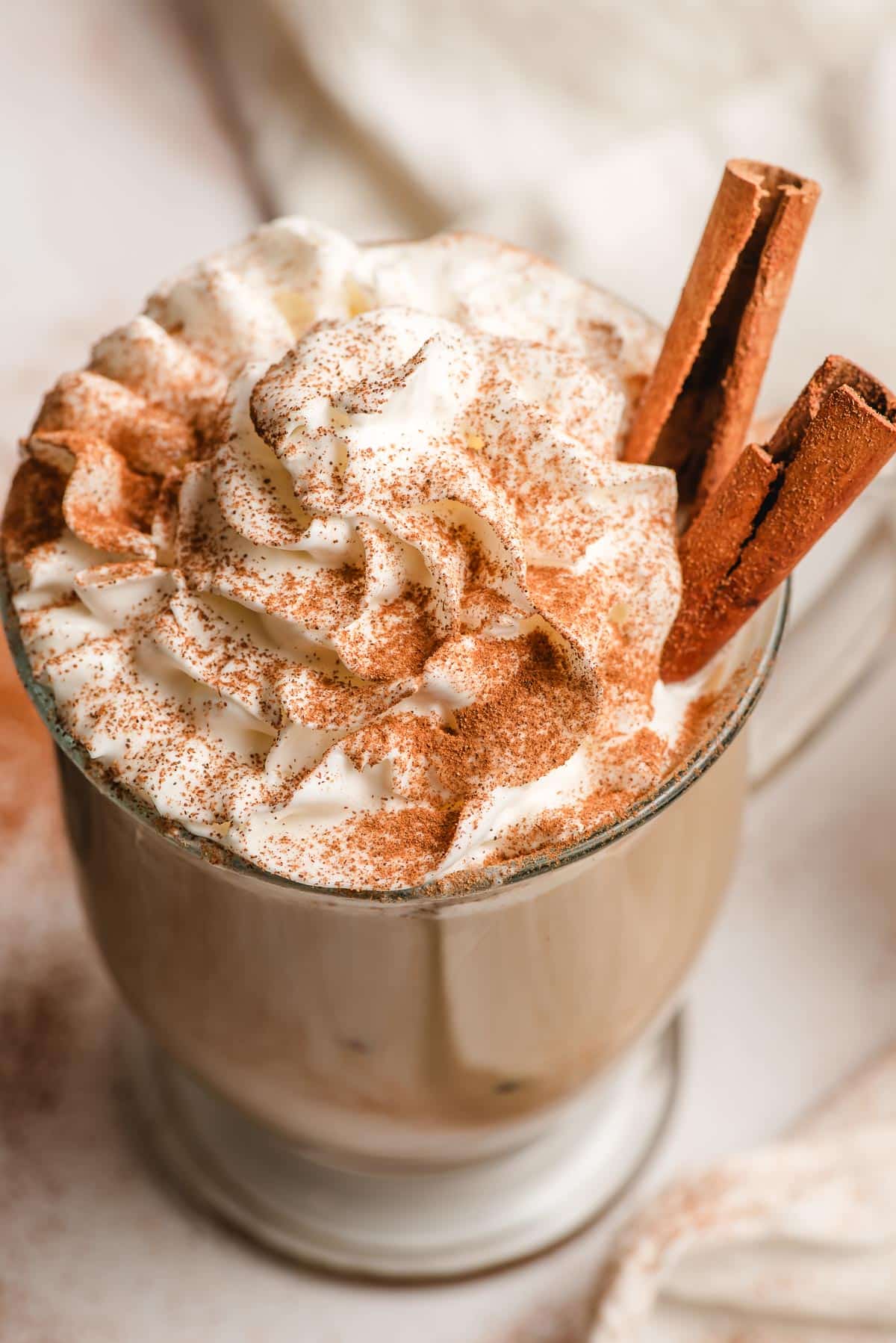 Billowy whipped cream topped with ground cinnamon on top of a cinnamon latte.