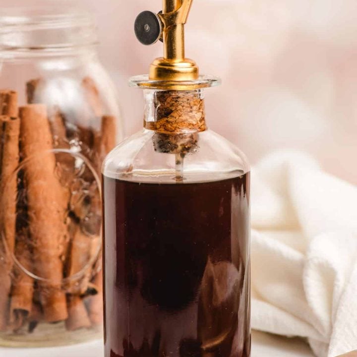 Glass oil bottle filled with brown sugar cinnamon syrup and surrounded by cinnamon sticks.