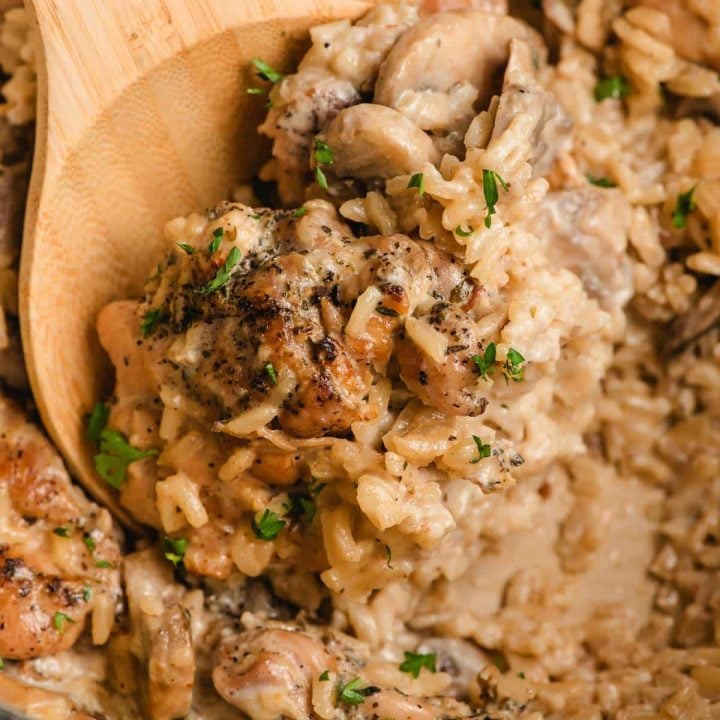 Wooden spoon scooping up creamy rice with chicken and mushrooms.