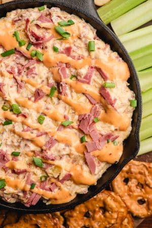 Hot reuben dip served in a cast iron skillet and topped with Thousand Island dressing and green onions.