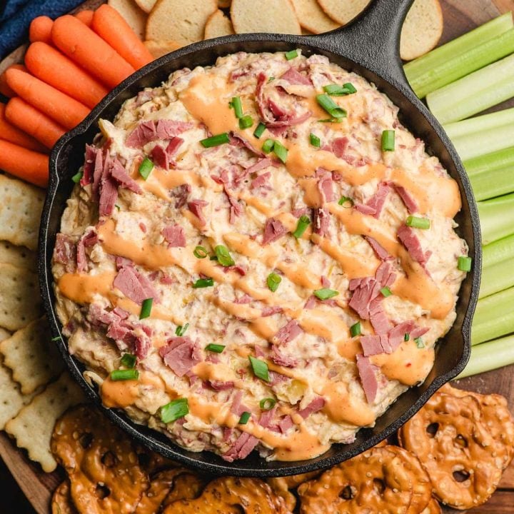 Slow cooker reuben dip served in a cast iron skillet, surrounded by crackers and chopped veggies.