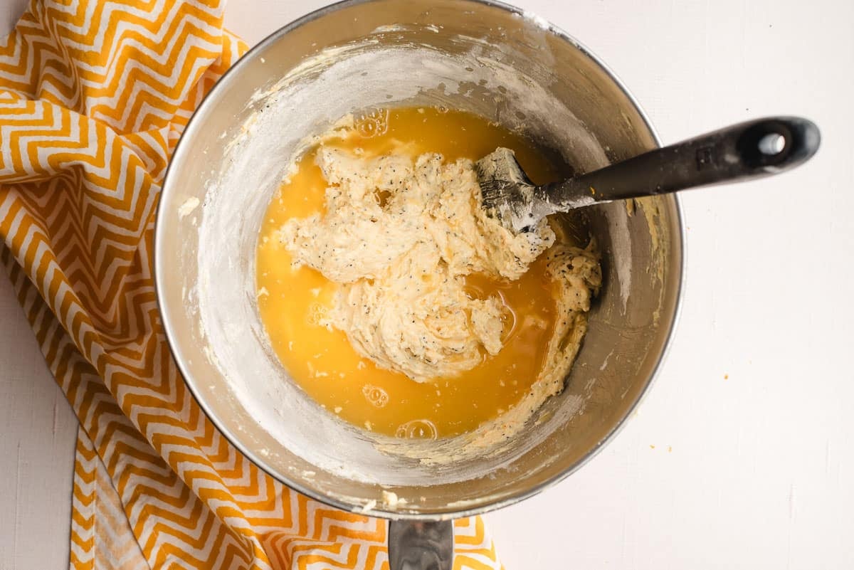 Orange juice poured into muffin batter in a stainless steel bowl.