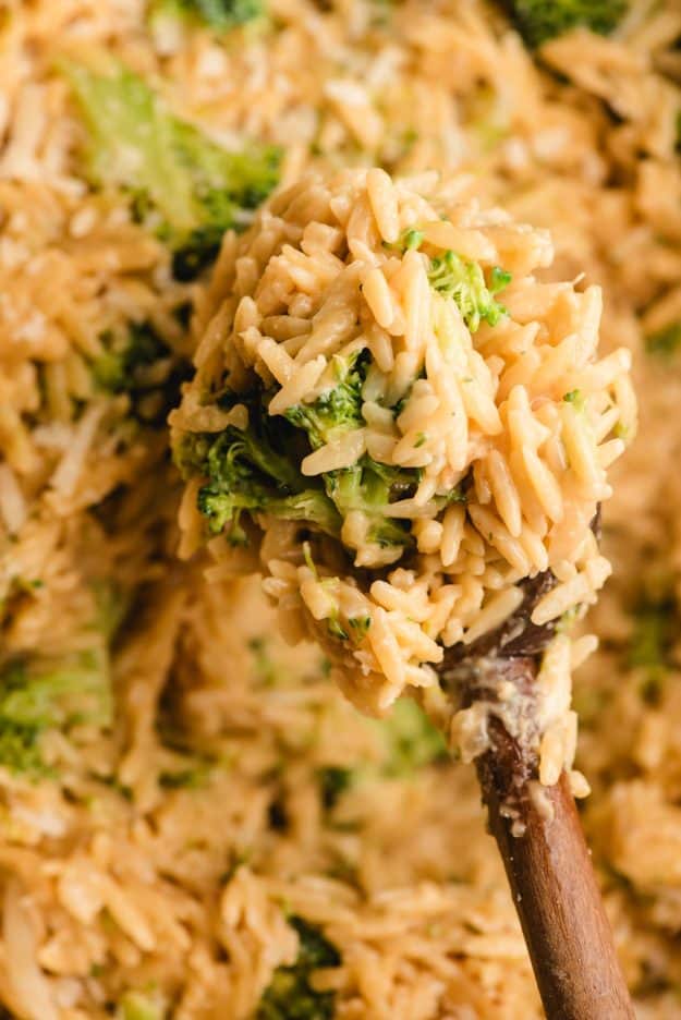 A wooden spoon scooping up cheesy orzo with broccoli.