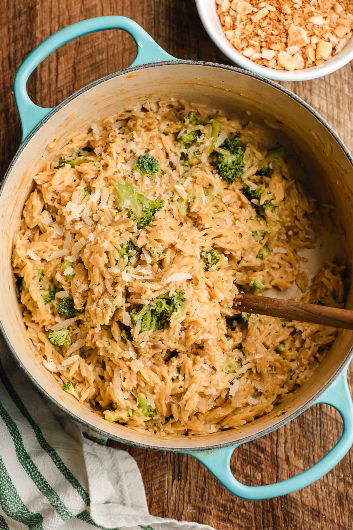 Broccoli cheddar orzo in a Dutch oven with a wooden spoon.