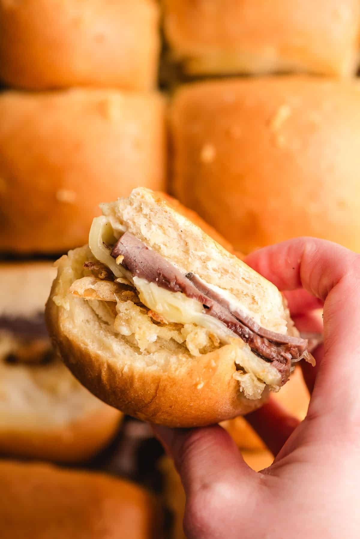 Hand holding a roast beef slider with french fried onions.
