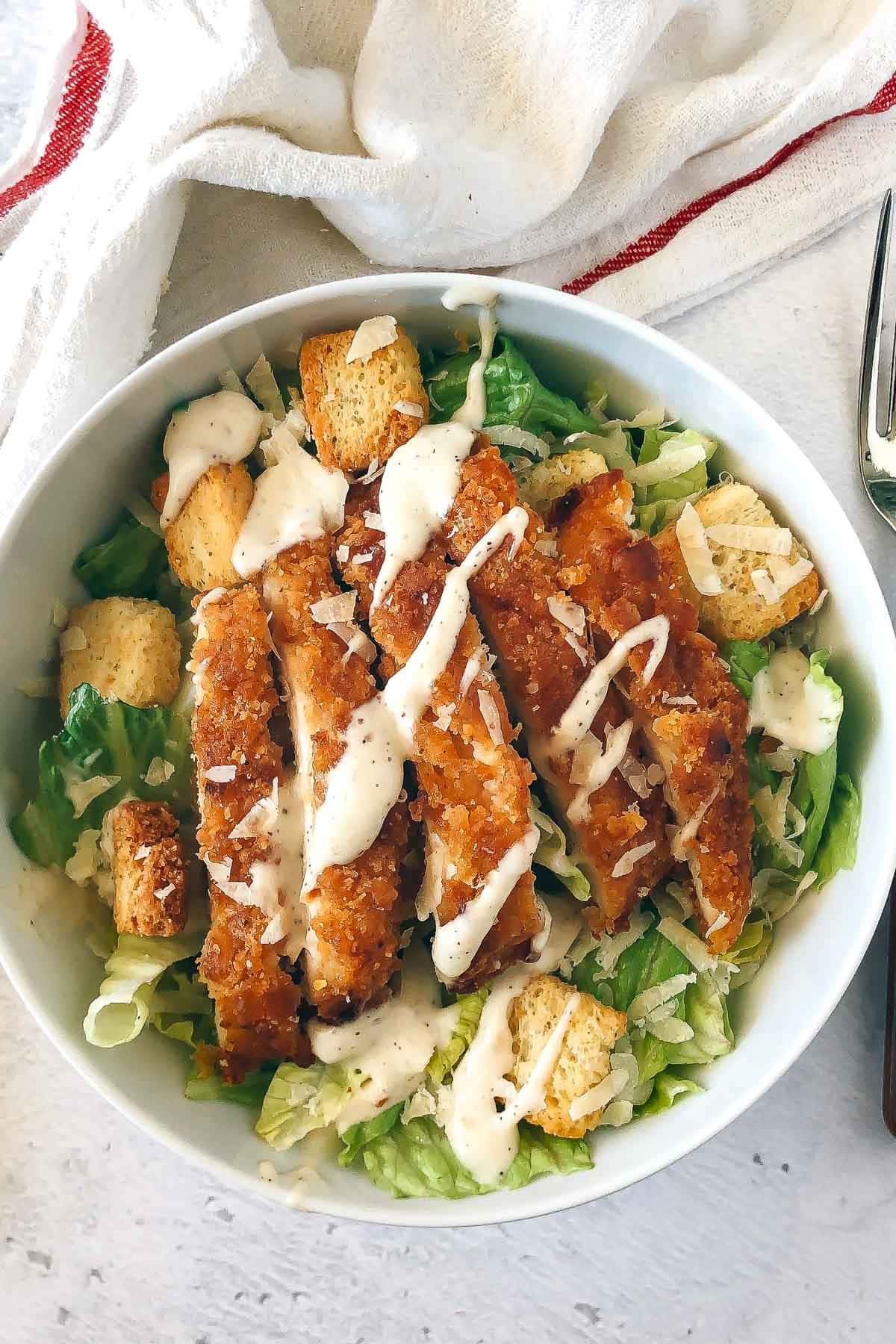 Breaded chicken on top of a Caesar salad kit.