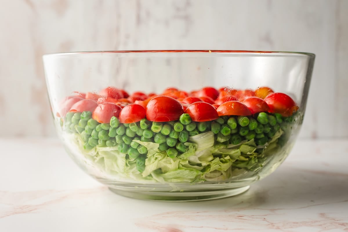 Lettuce, peas, and tomatoes layered in a bowl.