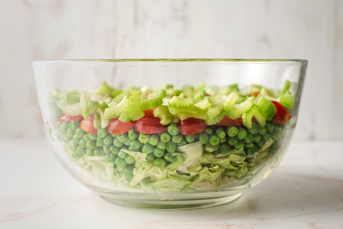 Glass mixing bowl with lettuce, peas, tomatoes, and celery.