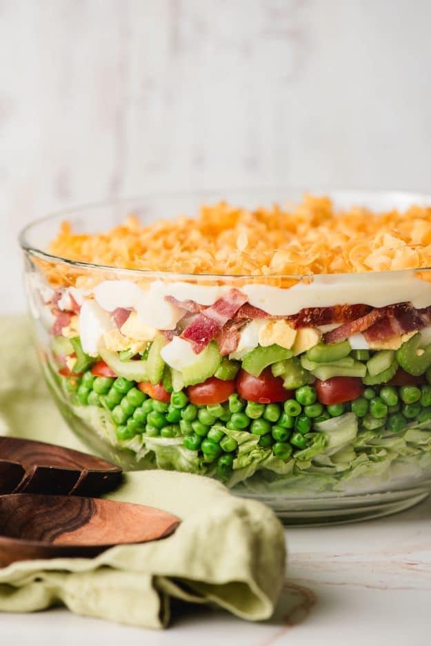 Close-up of 7 layer salad topped with shredded cheddar cheese and creamy dressing in a trifle bowl