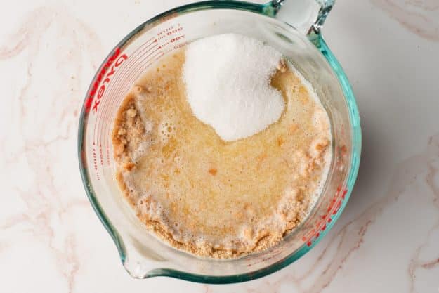 Butter, sugar, and graham cracker crumbs in a glass measuring cup.
