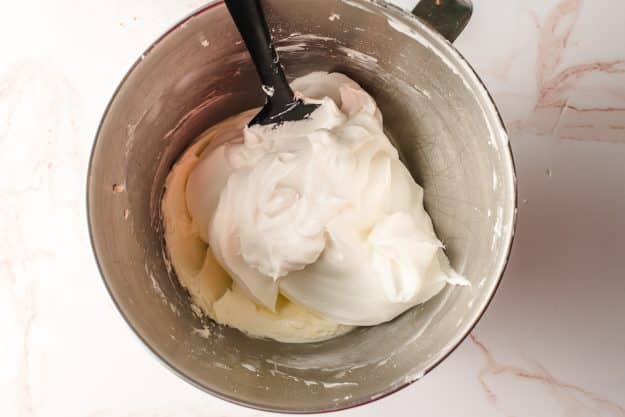 Cool whip being stirred into sweetened whipped cream.