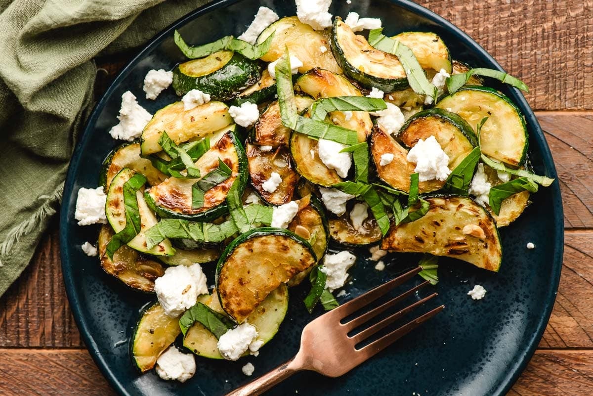 Sauteed zucchini with goat cheese, fresh basil, and lemon zest on a blue plate.