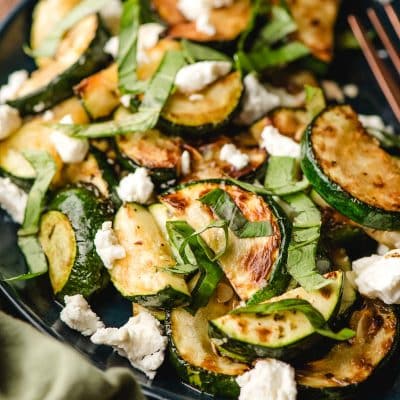 Zucchini saute with goat cheese and fresh basil on a navy blue plate.