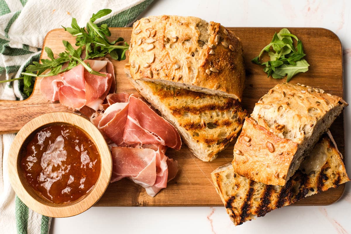 Grilled bread on a cutting board with prosciutto and apricot jam.