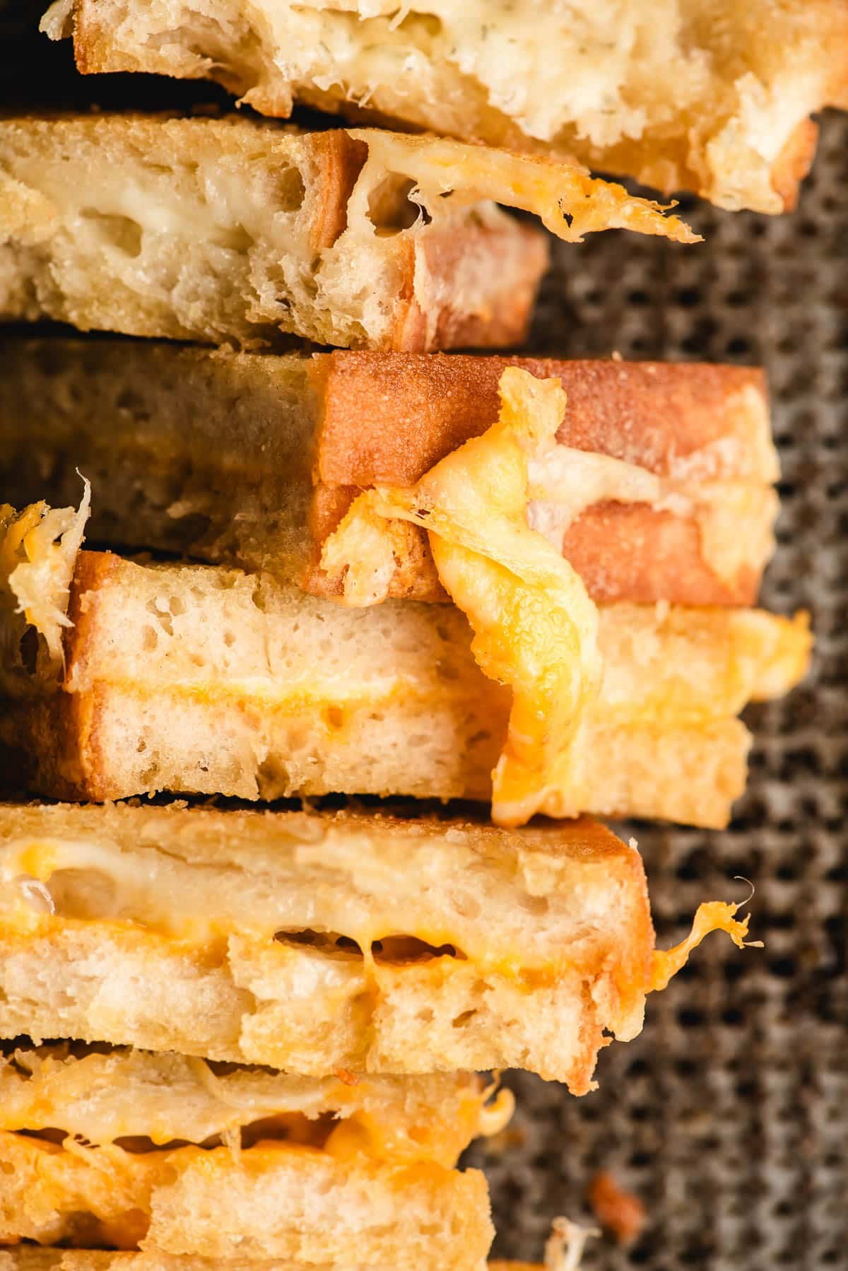 Halved grilled cheese sandwiches with string of gooey cheese pouring out.