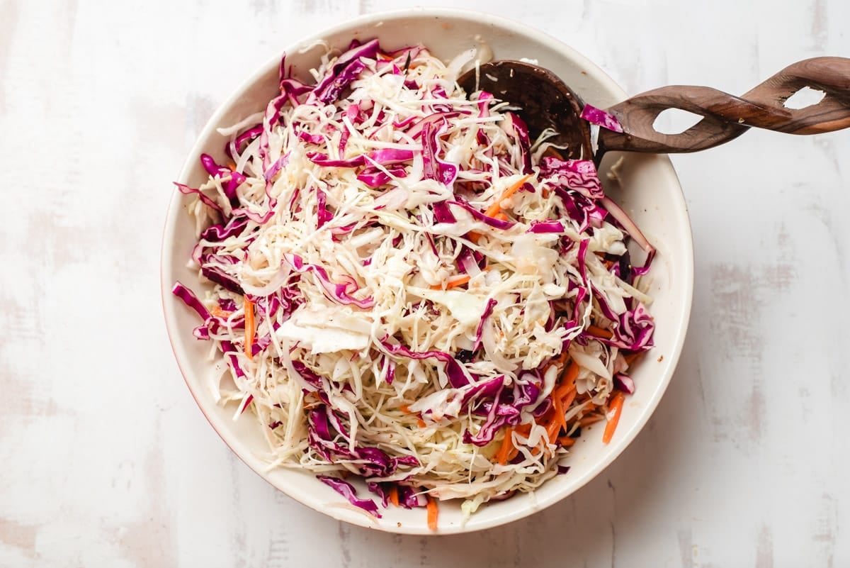 Big bowl of sweet and sour coleslaw with wooden spoon.