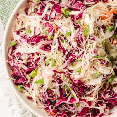 Bowl of sweet vinegar coleslaw with green onions on top.