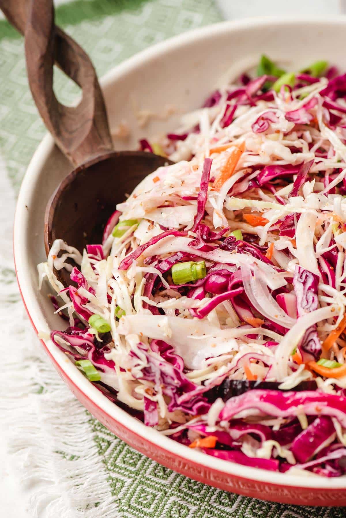 Sweet and sour coleslaw in a big bowl with a wooden serving spoon.