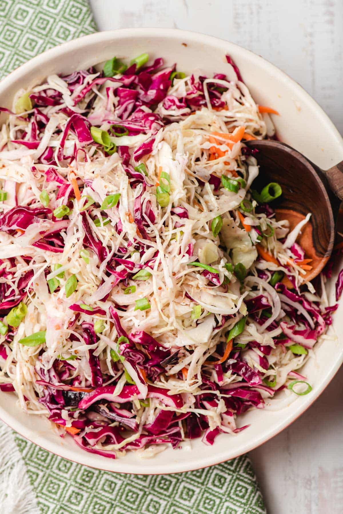 Sweet and sour coleslaw in a serving bowl with a wooden spoon.