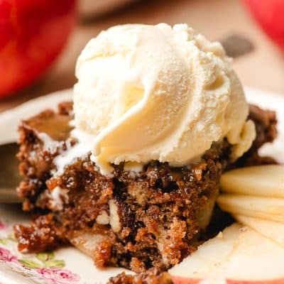 Scoop of vanilla ice cream melting down the side of a slice of apple dapple cake.