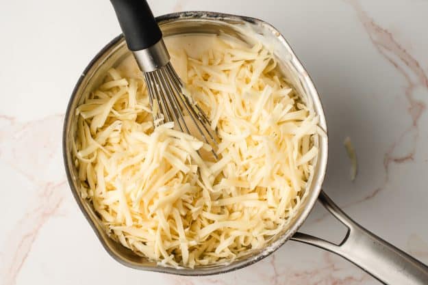 Shredded cheese being added to a cream sauce.