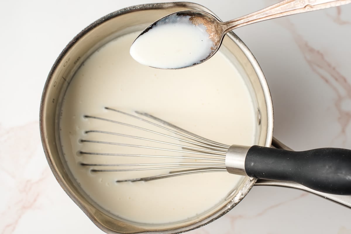 Spoon holding a cream sauce over a sauce pan.