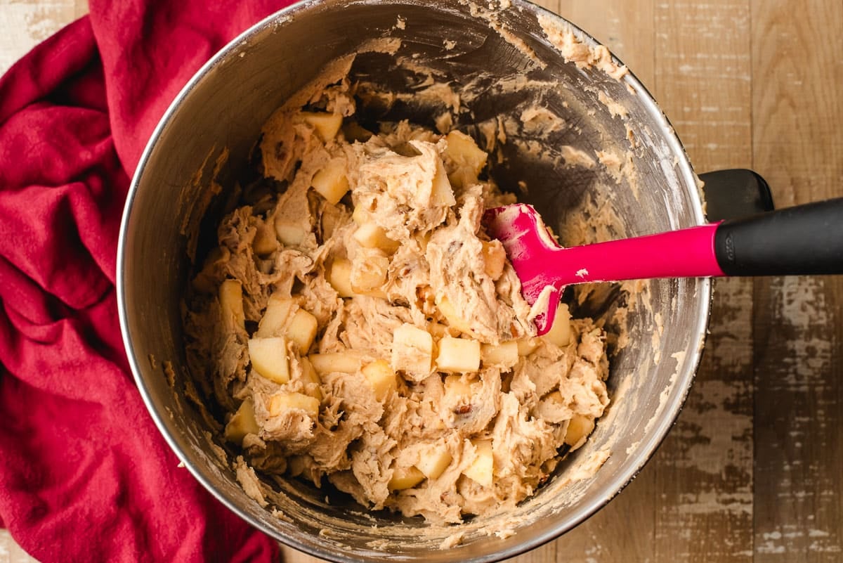 Apples and pecans stirred into spiced cake batter in a bowl.