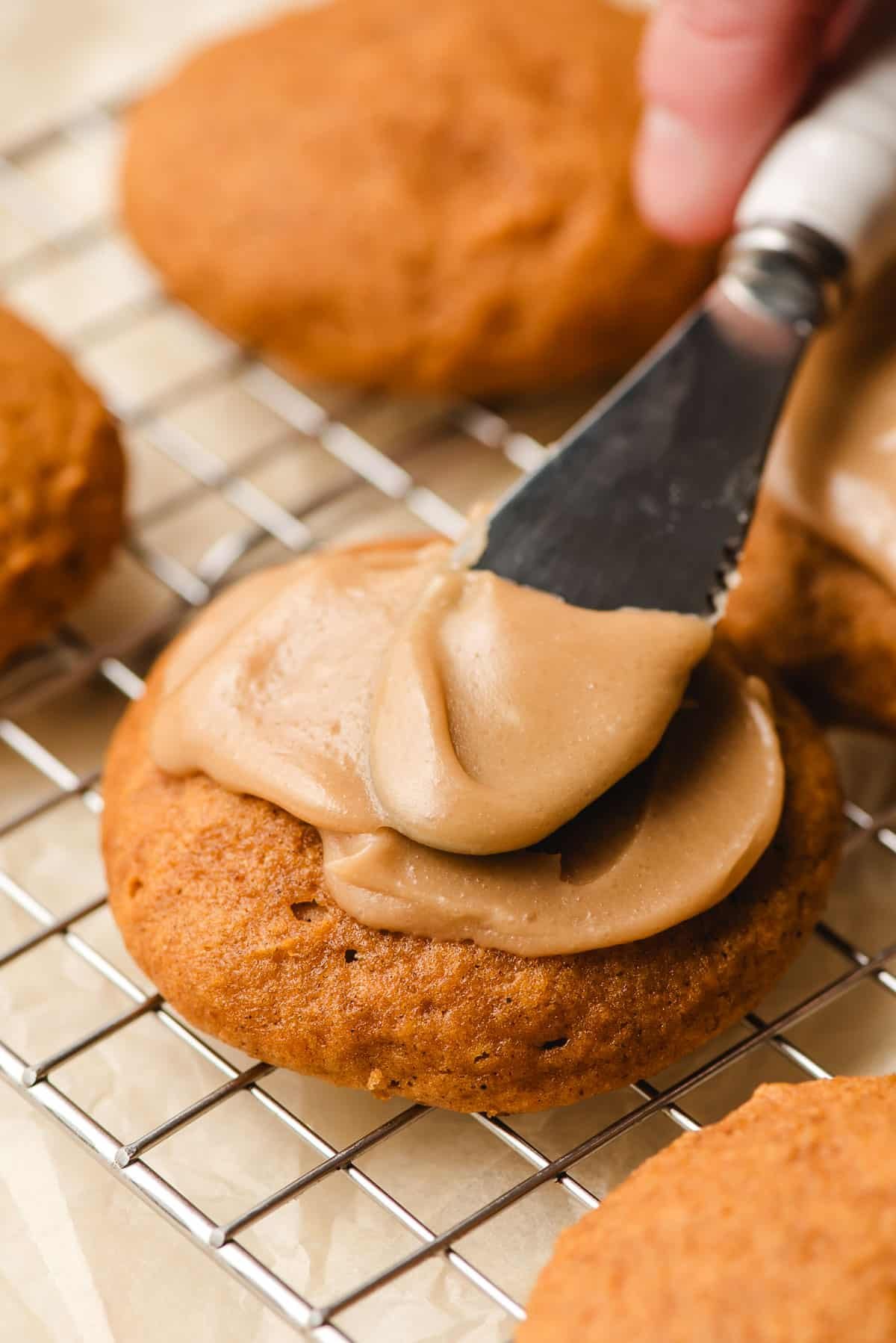 Penuche frosting being spread on soft pumpkin cookies.