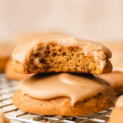 Stack of frosted pumpkin cookie with a bite taken out of the top one.