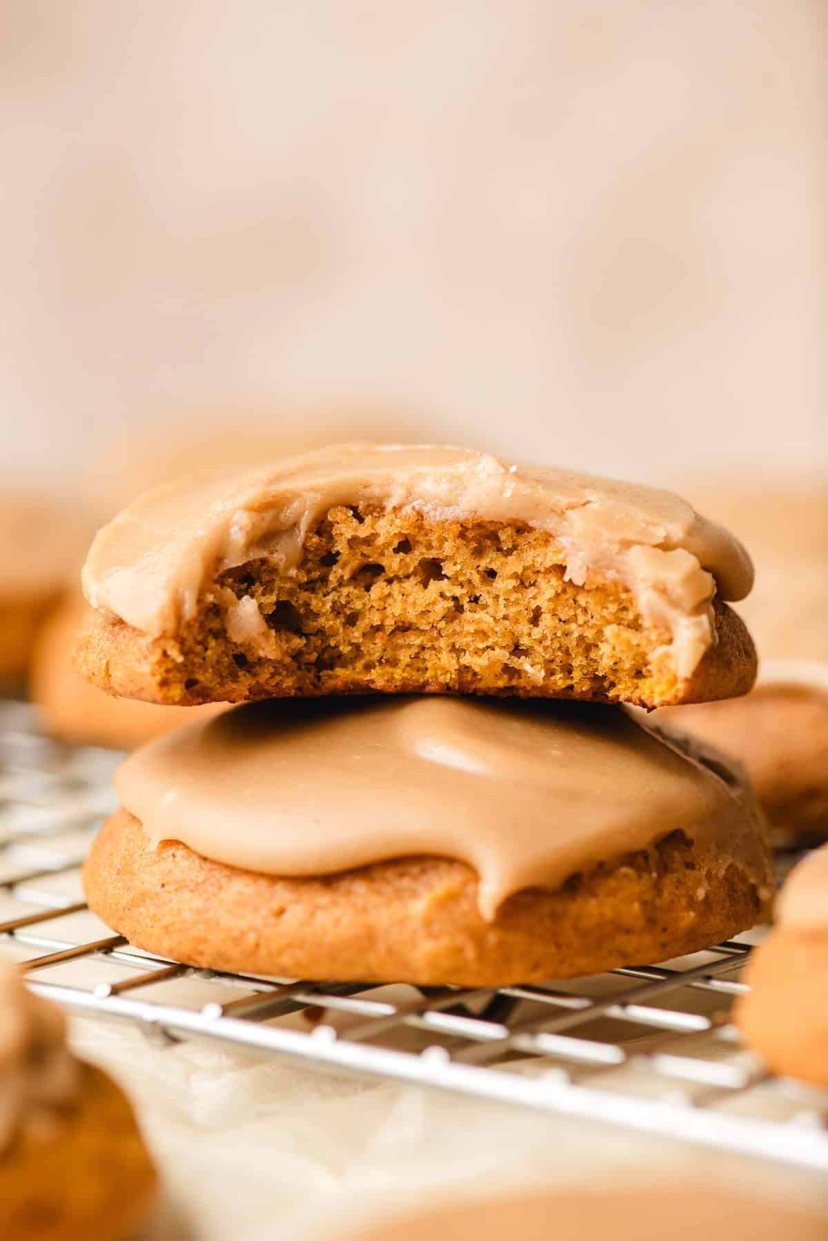 Stack of frosted pumpkin cookie with a bite taken out of the top one.