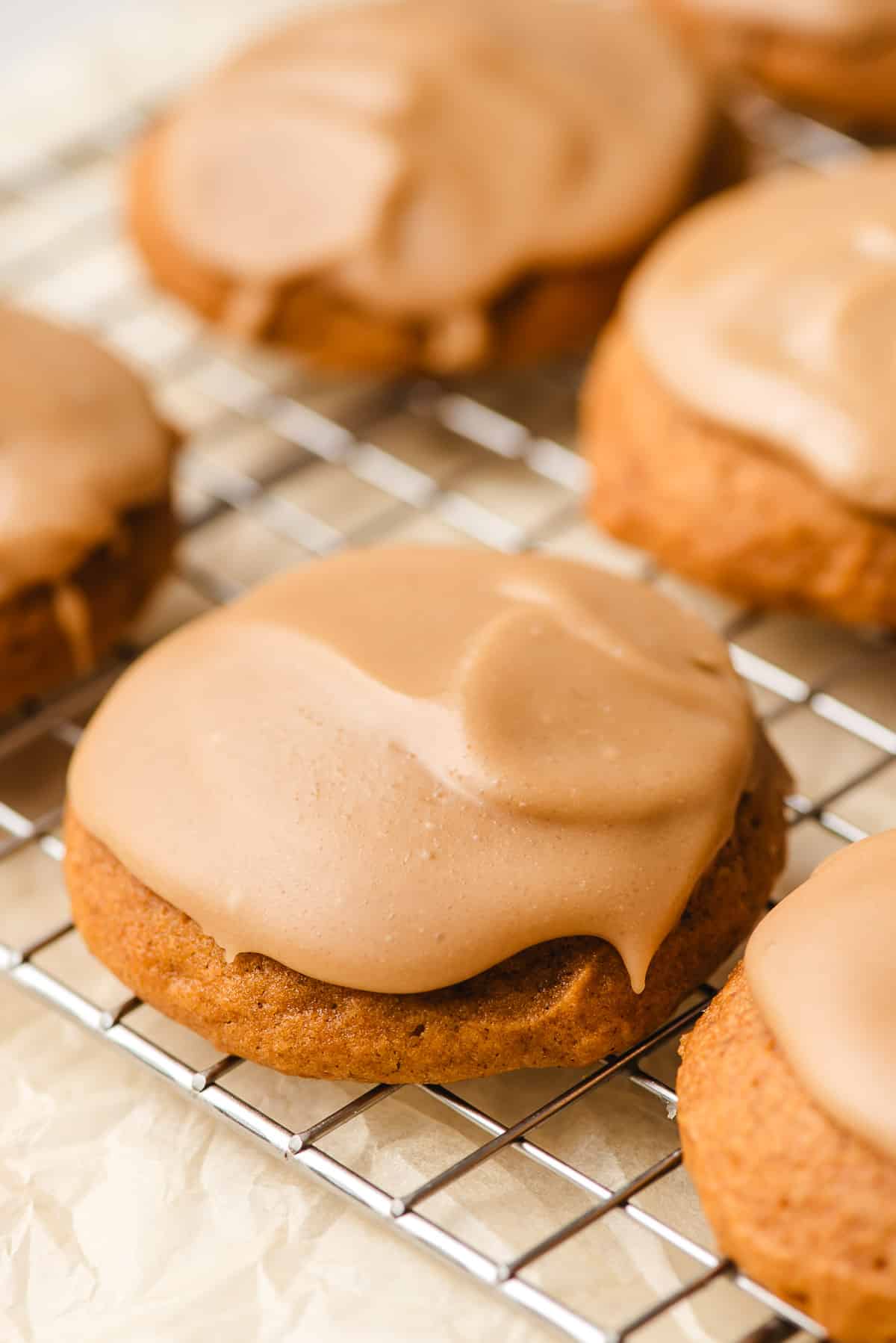 Frosted pumpkin cookies on a wire cooling rack.