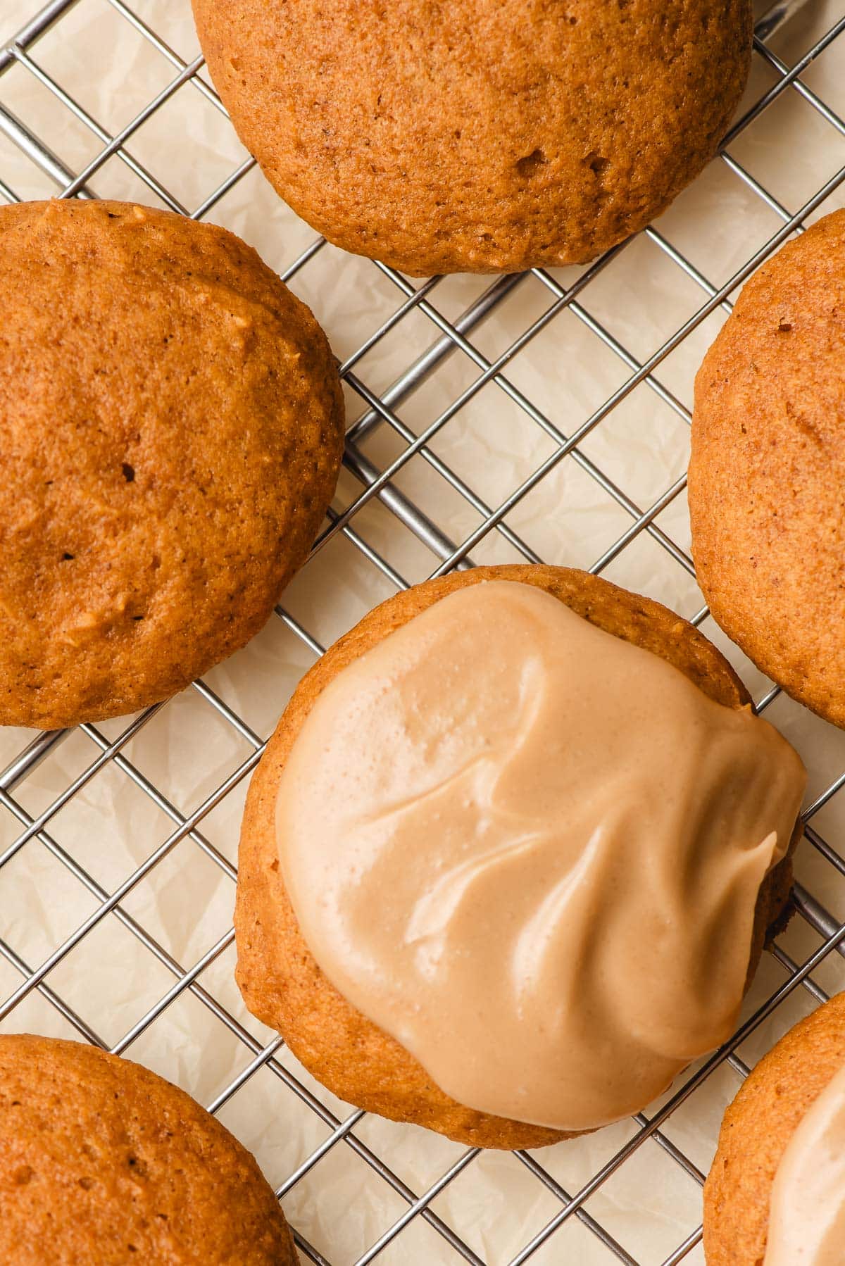 One frosted pumpkin cookie on a wire rack with other unfrosted cookies.