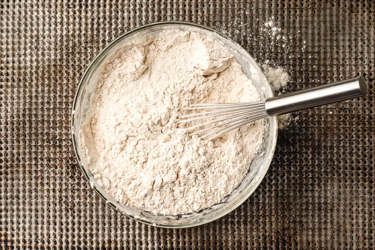 Flour, baking soda, baking powder, and pumpkin spices whisked together in a glass bowl.