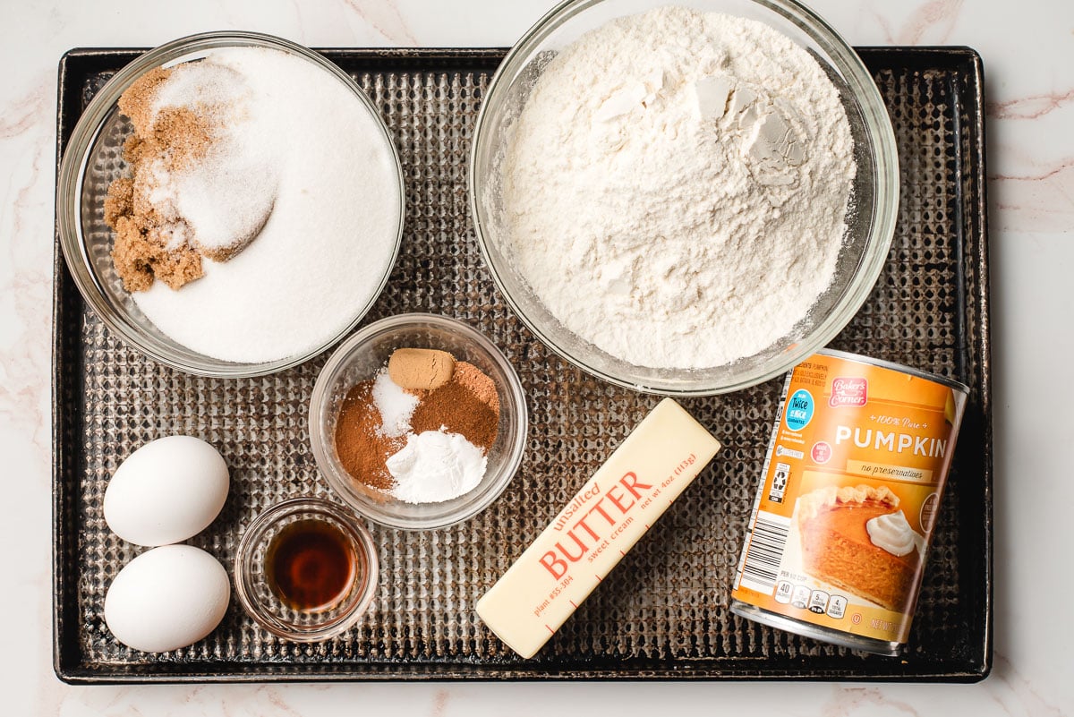 Bowls of sugar, flour, baking soda, salt, and spices, eggs, vanilla, butter, and pumpkin puree.