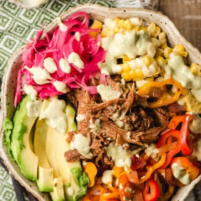 Scalloped bowl filled with rice, pulled pork, avocado, bell pepper, corn, and pickled cabbage and onions, drizzled with avocado dressing.