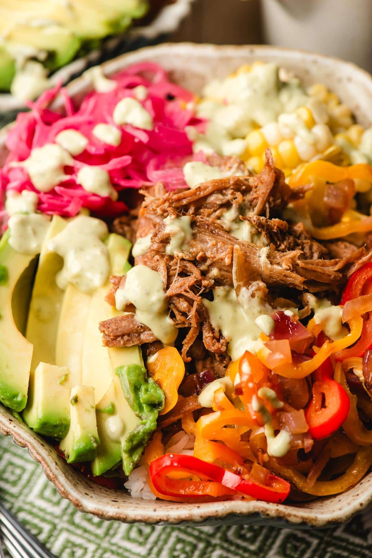 Pulled pork rice bowls topped with avocado, peppers, onions, and corn and drizzled with green avocado dressing.