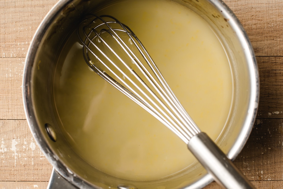 Lemon glaze in a sauce pot with a metal whisk.