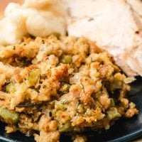 Scoop of stuffing on a plate next to mashed potatoes and sliced turkey.