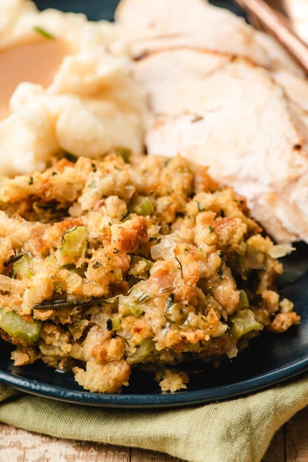 Scoop of stuffing on a plate next to mashed potatoes and sliced turkey.