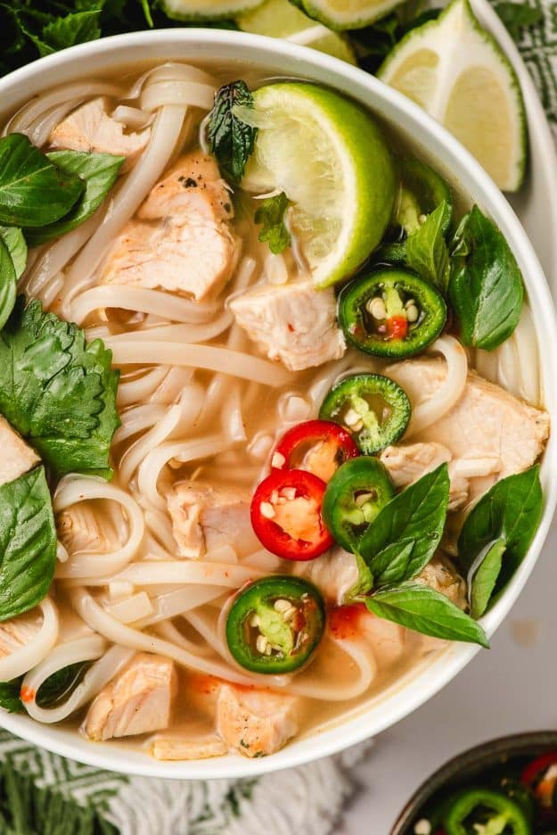 Turkey pho in a bowl with sliced jalapenos, mint, and lime wedges.