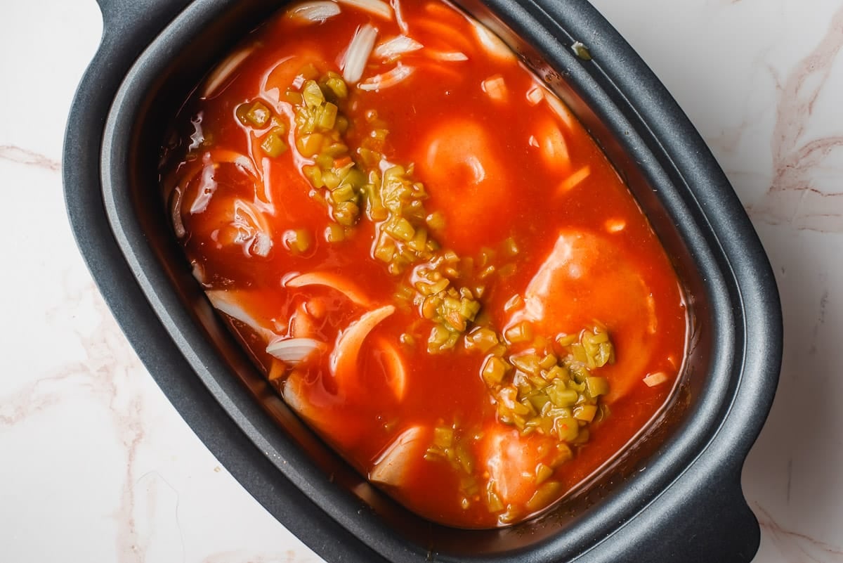 Chicken breast covered in enchilada sauce, green chilies, and seasonings in the crock pot.