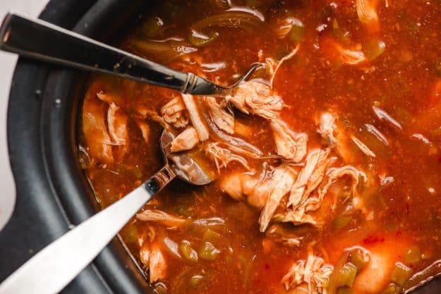 Two forks shredding enchilada chicken in a slow cooker.