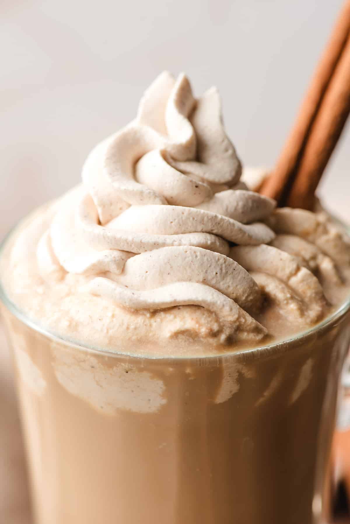 Swirled cinnamon whipped cream on top of a latte in a glass mug.