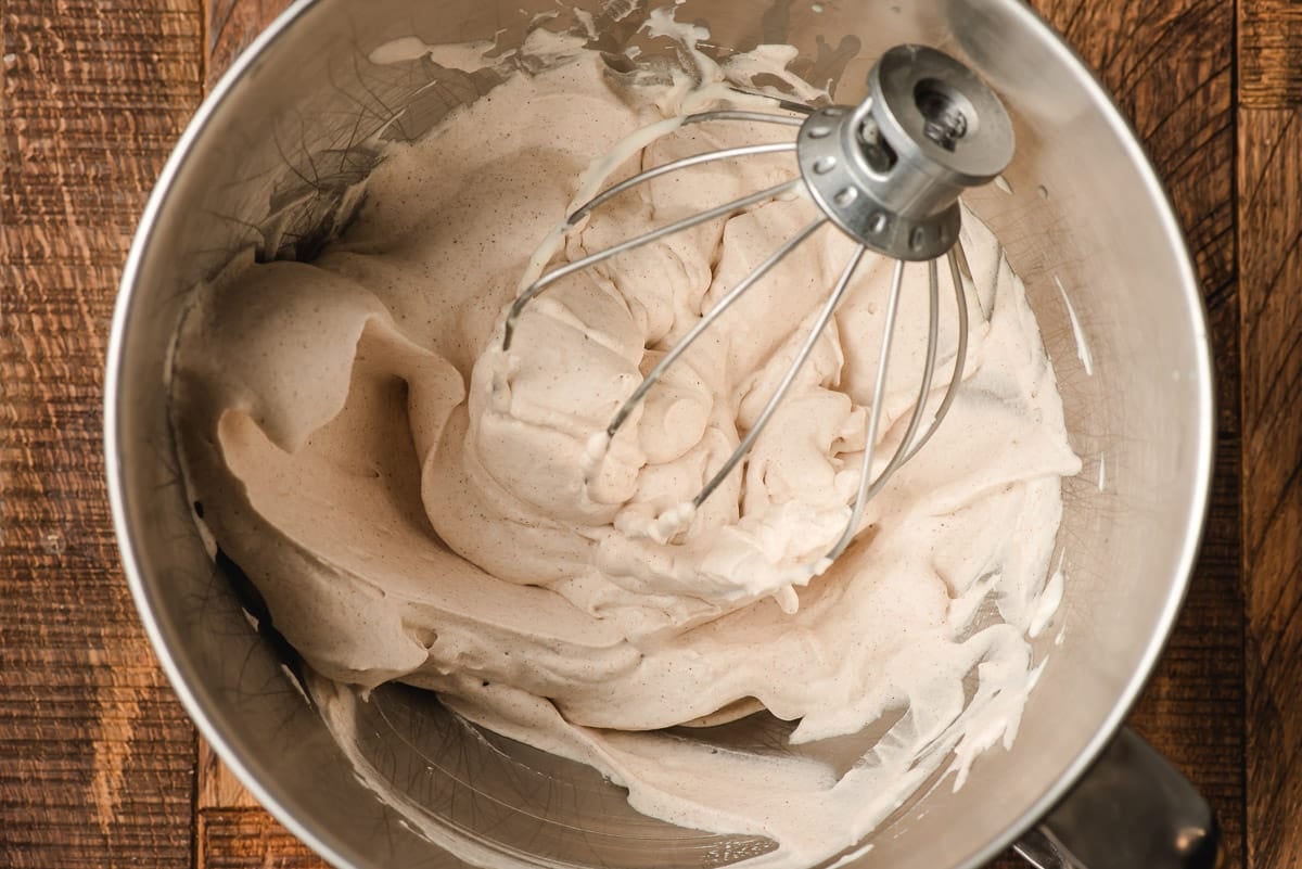 Whipped cinnamon cream in the bowl of an electric mixer.