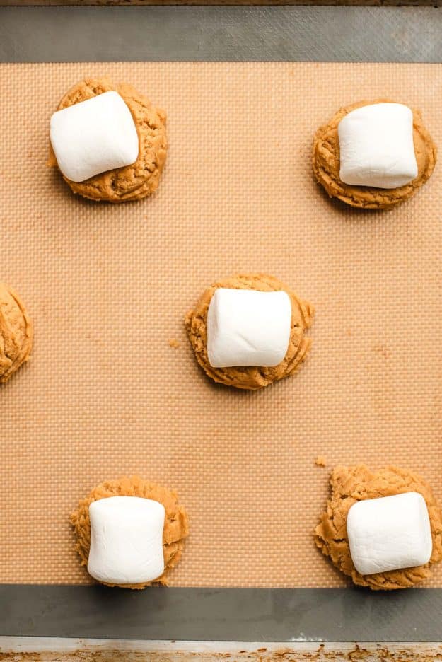 Baking sheet full of peanut butter cookie dough balls with a marshmallow pressed into the top.