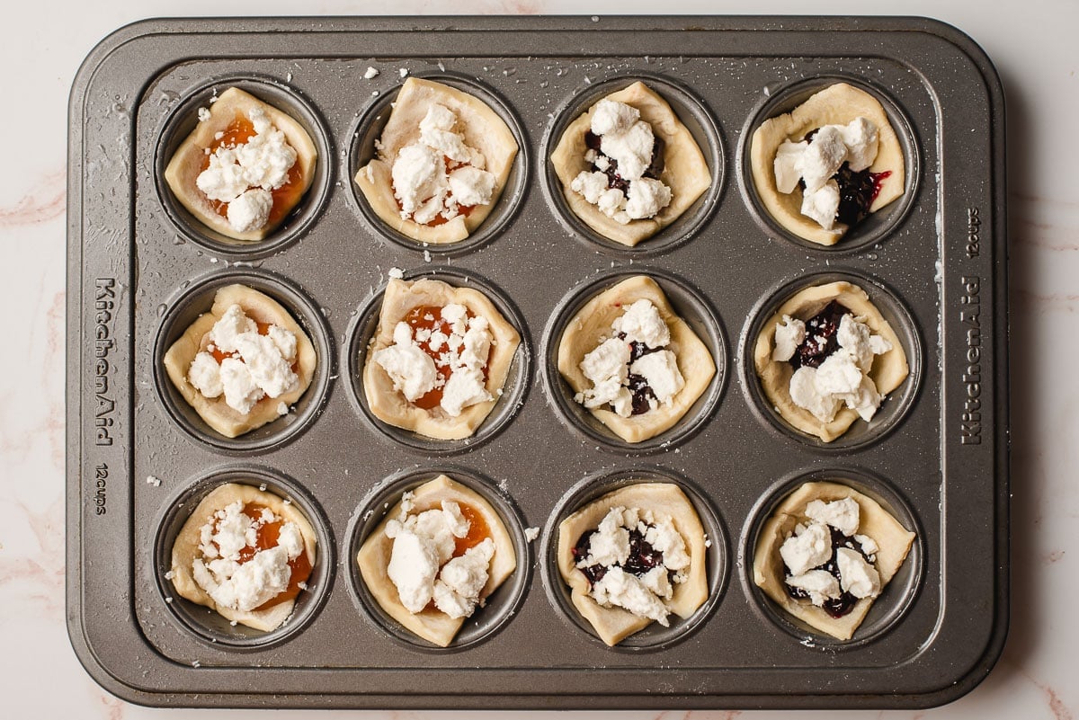 Mini muffin tray filled with puff pastry and goat cheese, unbaked.