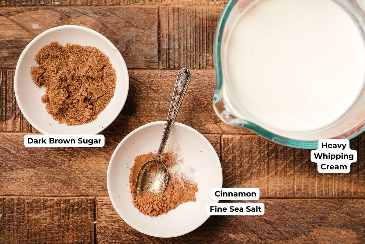 Bowls of cinnamon, dark brown sugar, and heavy whipping cream on a wood background