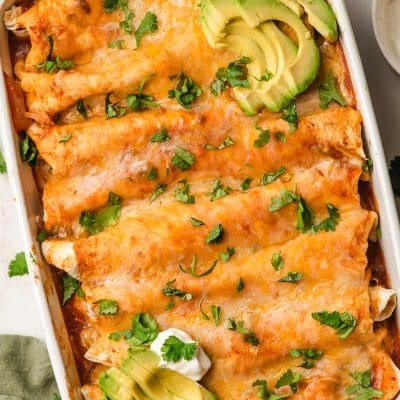 Cheesy chicken enchiladas with cilatnro and avocado in a casserole dish.